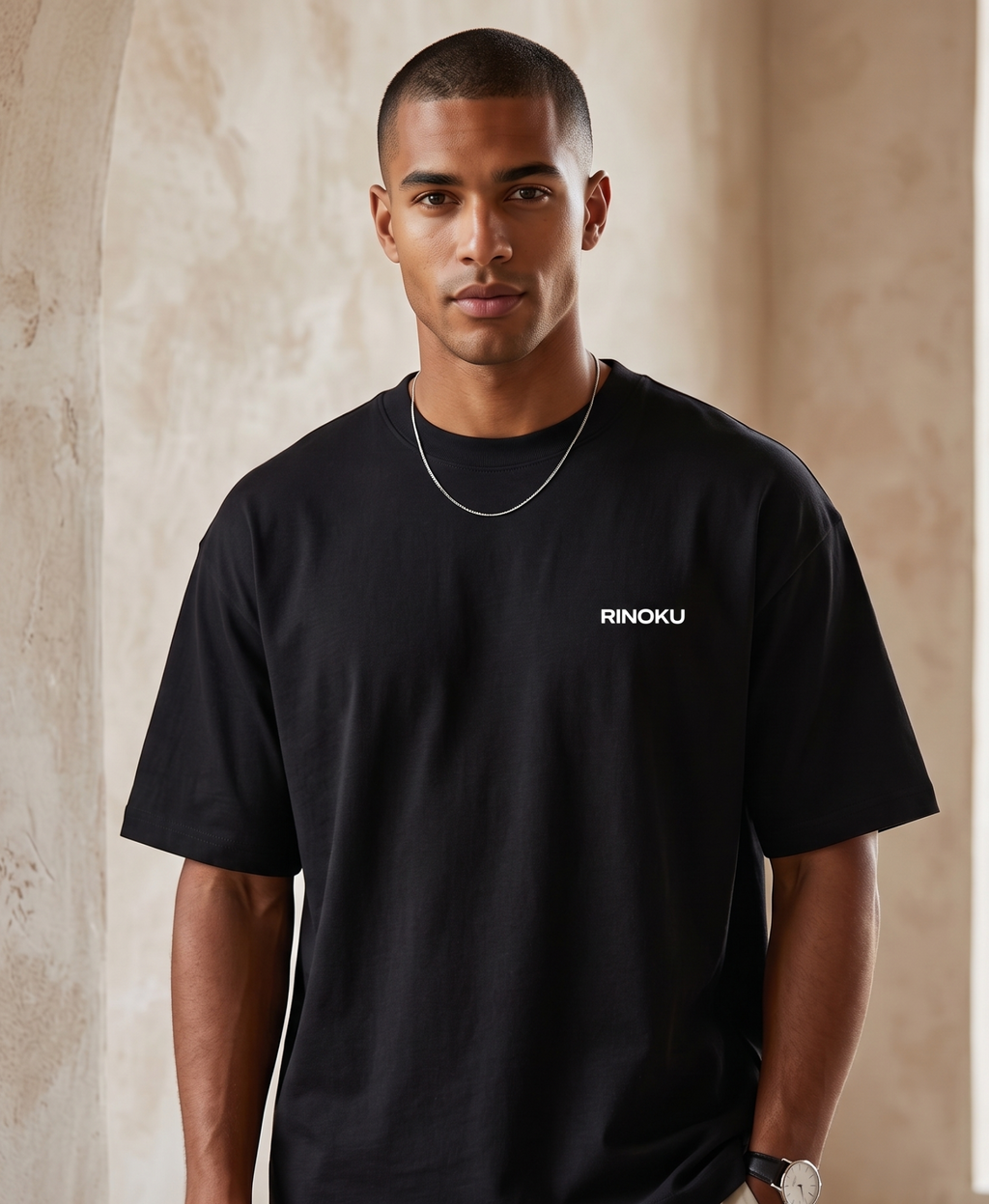 Man wearing a black t-shirt with 'RINOKU' logo against a beige wall